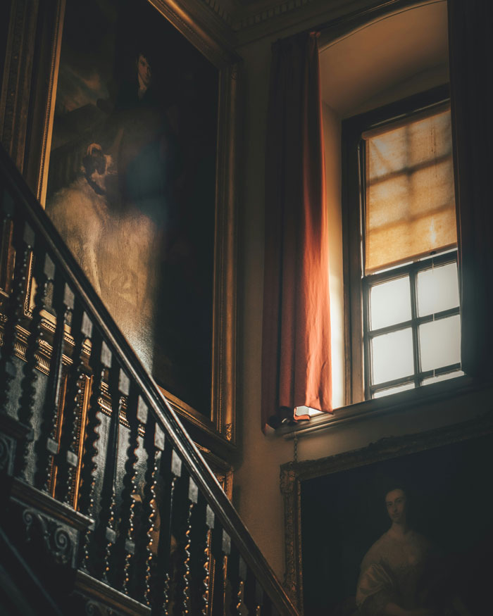 Ornate staircase and vintage paintings inside a dimly lit rich estate, revealing unexpected things about the rich.