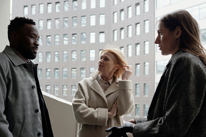 Three people having a serious conversation outdoors in an urban setting, reflecting diverse perspectives on microfeminisms.