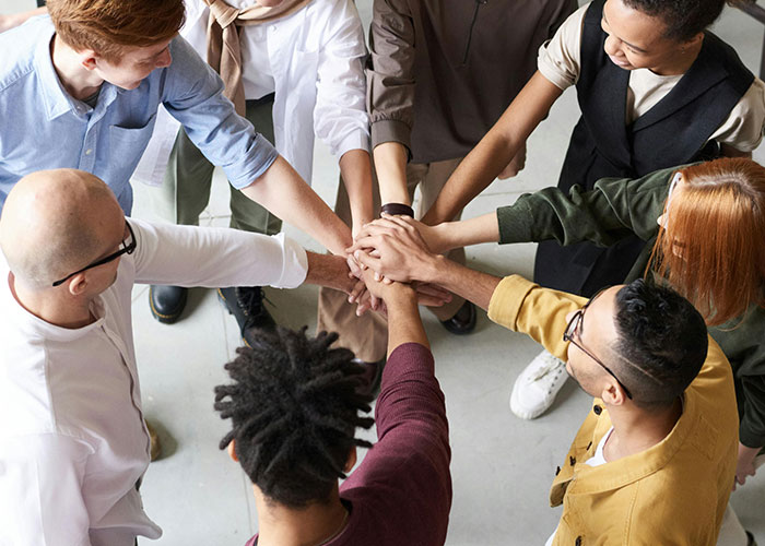 Diverse team joining hands in a circle, symbolizing teamwork and unity in a workplace without micromanagement.