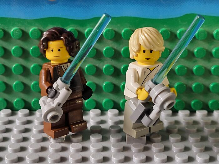 Two LEGO characters holding blue lightsabers on a textured green and gray base, evoking medical professionals’ shock.