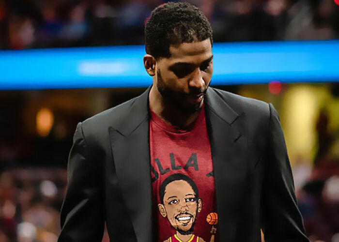 Man wearing a graphic t-shirt and black blazer, with a blurred crowd background, related to KarJenner clan controversies. - 14