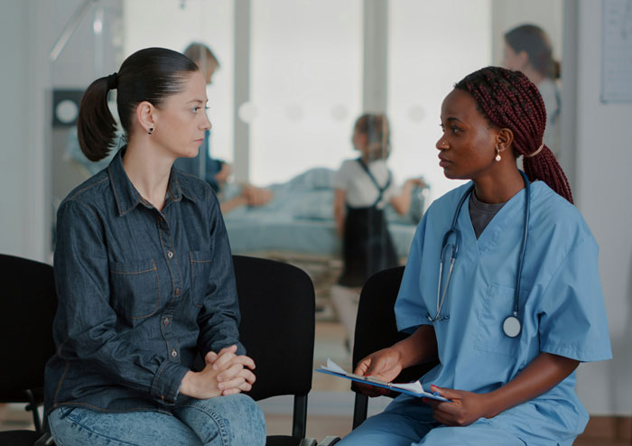 Medical professional in blue scrubs discussing patient privacy concerns with woman in a clinical waiting area. - 3