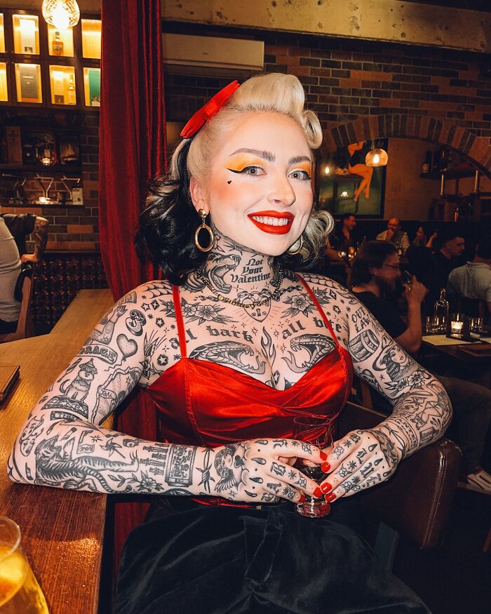 Woman with extensive tattoos showcasing her body suit transformation, smiling confidently in a vibrant red outfit. - 7