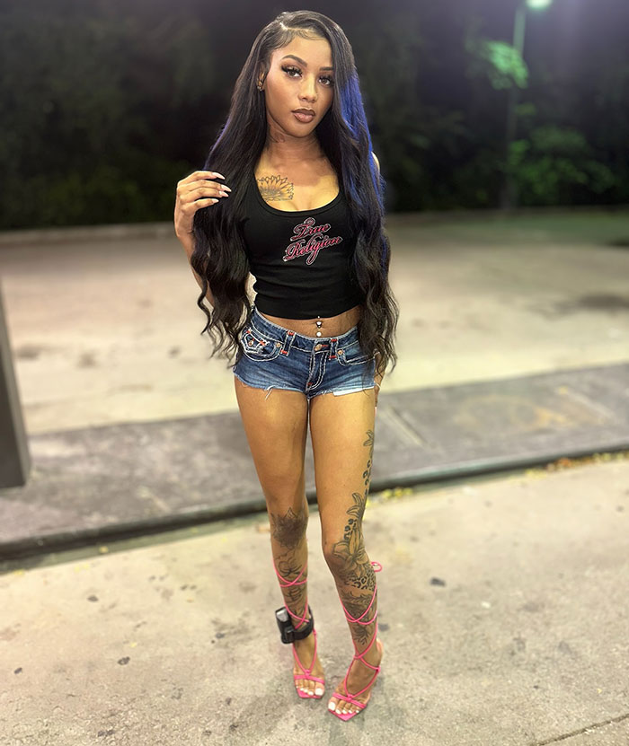 Young woman with long hair, tattoos, and denim shorts posing outdoors, linked to former reality TV child star news.