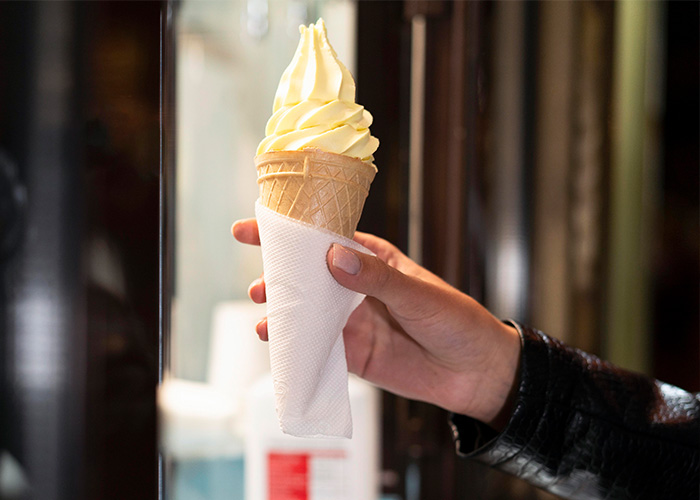 Hand holding a soft serve ice cream cone wrapped in a white napkin, illustrating former employees’ crazy secrets. - 1