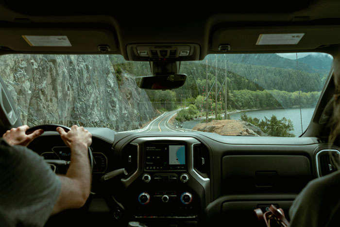 View from inside a vehicle driving along a winding road by cliffs and a lake, evoking real-life horror stories. - 3