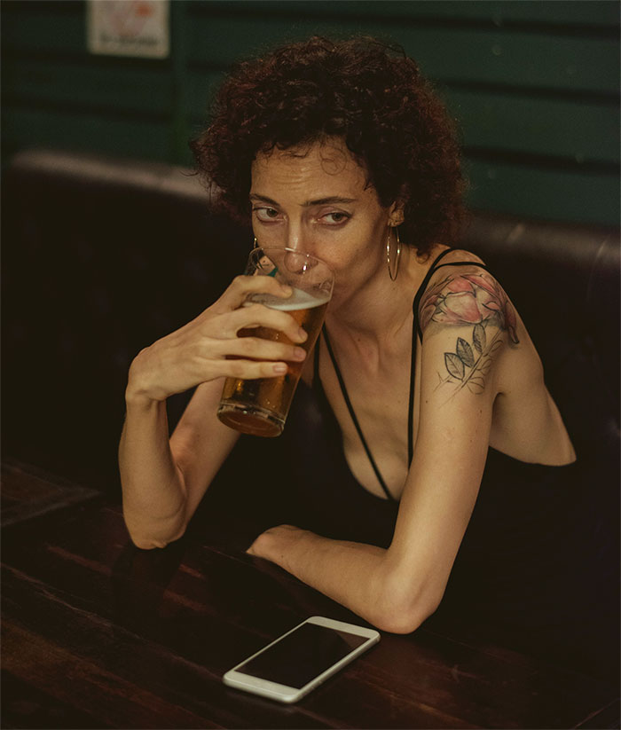 Woman with tattoo drinking beer at a bar looking thoughtful about guy's female best friend and surprise birthday party conflict - 5