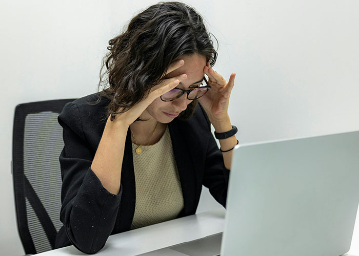 Woman stressed at desk with laptop showing signs of micromanagement in a challenging workplace environment.