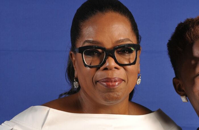 Close-up of a woman wearing large black glasses and white attire, symbolizing the journey from poverty to super wealthy.