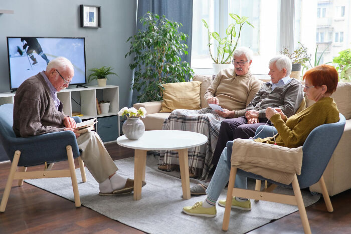Group of elderly people sitting in living room, reading and knitting, reflecting on thank you notes and old traditions fading away.