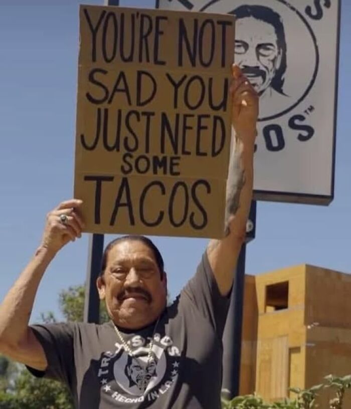 Hispanic man holding a sign about tacos outdoors, capturing funny memes that sum up Hispanic cultural humor.