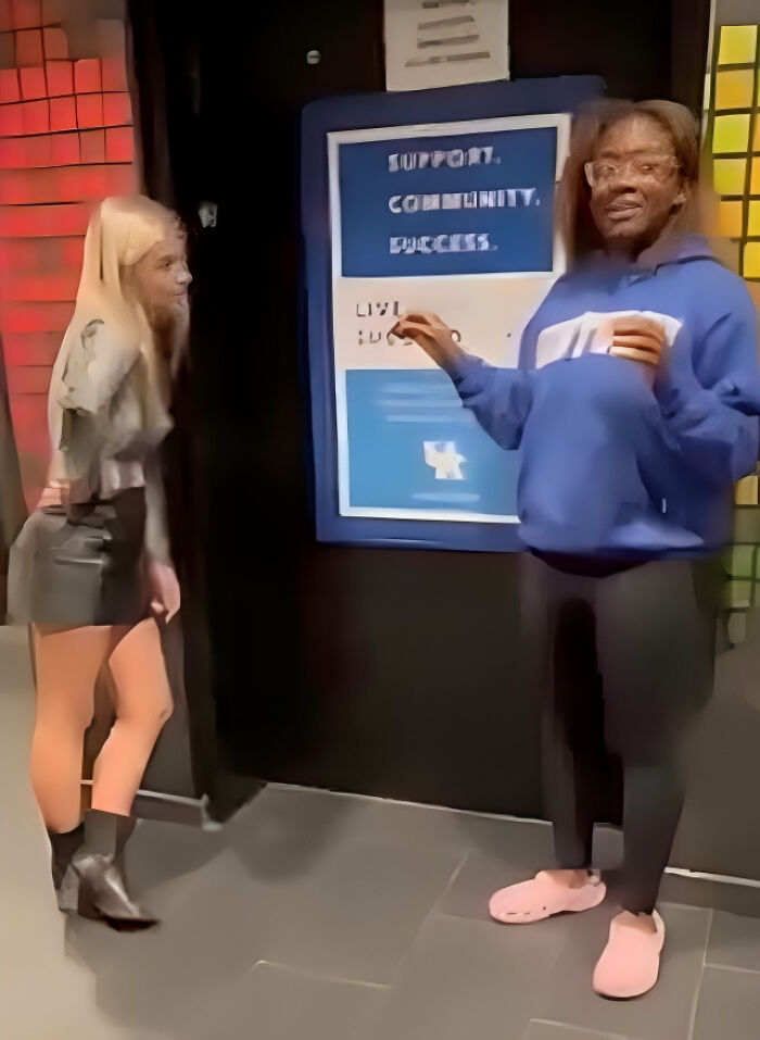 Two people standing and talking near a sign in a hallway showing consequences of their own stupidity at work.