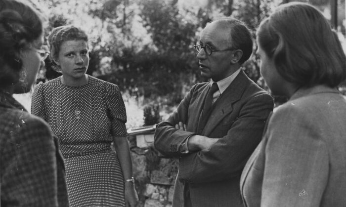 Group of people in discussion outside a school during World War II, capturing schools worldwide history.