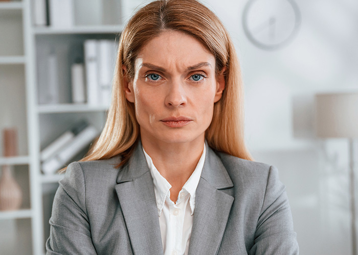 Serious businesswoman in gray suit frowning while addressing ridiculous complaints from employees in office setting.