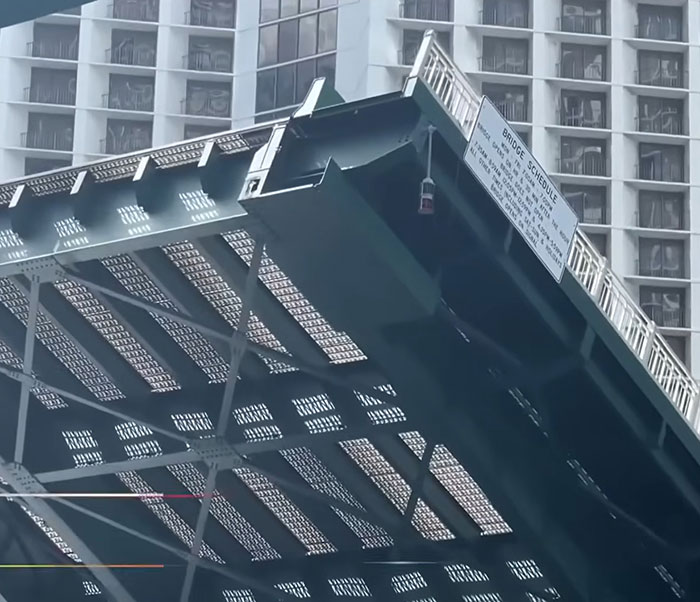 Close-up of a rising drawbridge with a warning sign, related to a woman surviving after holding on for dear life. Close-up of a rising drawbridge with a warning sign, related to a woman surviving after holding on for dear life.