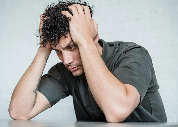 Young man with curly hair holding his head in frustration, reflecting on one of the worst cheating stories.