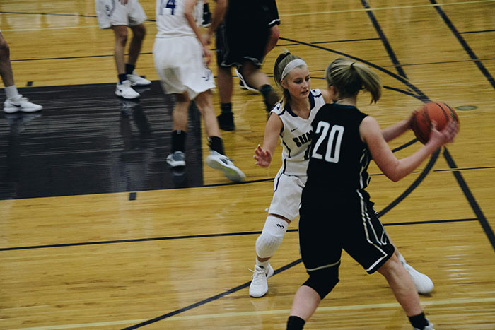 Two female basketball players on court competing during a fast-paced game in an indoor gymnasium setting.