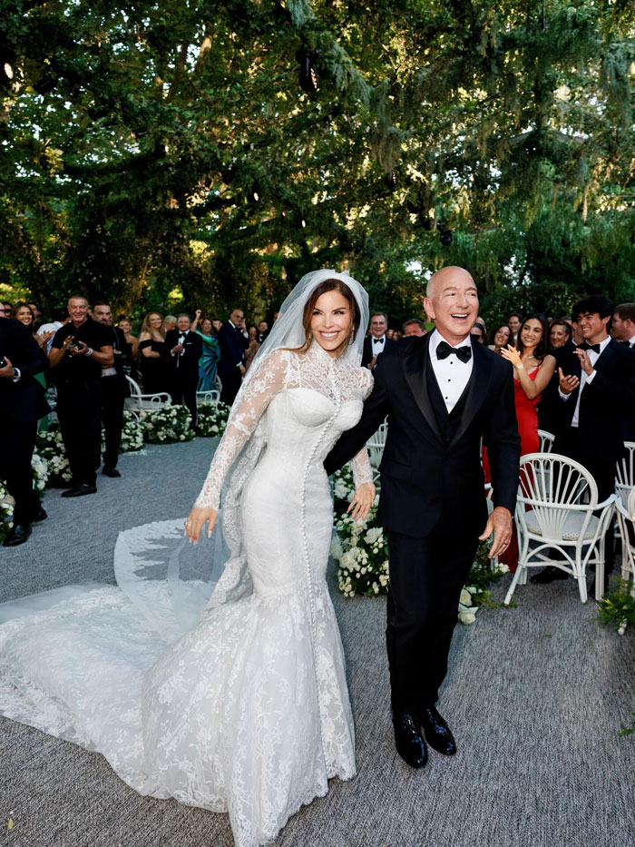 Jeff Bezos in a tuxedo with full hair, walking with bride Lauren S&aacute;nchez at their outdoor wedding ceremony.