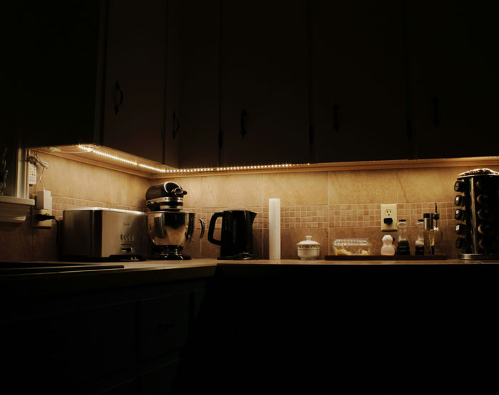 Dimly lit kitchen corner with under-cabinet lights, showcasing appliances and creating a real-life horror story atmosphere. - 14