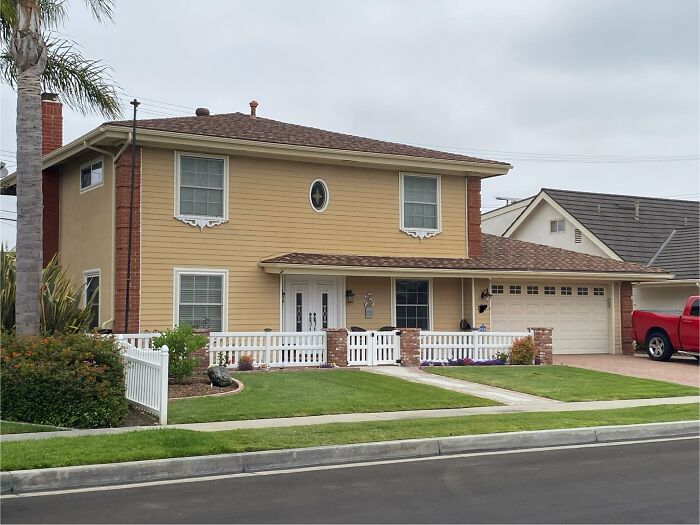 Two-story house with mismatched window styles and a small white fence in a suburban neighborhood, creative home design fail.