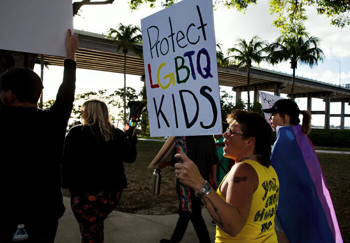 Protester holding a sign to protect LGBTQ kids during a demonstration highlighting consequences of their own stupidity at work.