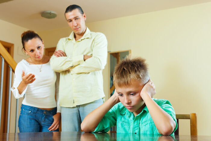 A stressed boy covering his ears while parents discuss, illustrating changing family communication from thank you notes era.