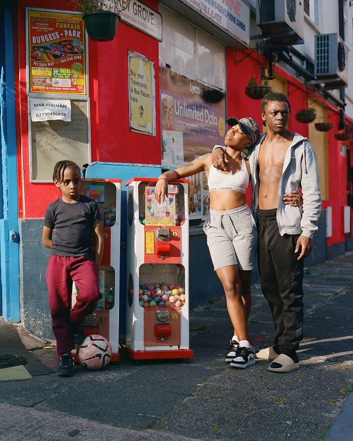 Three young people on a London street posing near vending machines in an honest photo by Nico Froehlich.