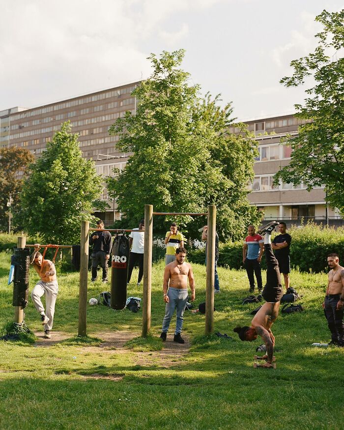 Men exercising in an urban green space with workout bars and boxing bags, capturing honest photos of London street life.