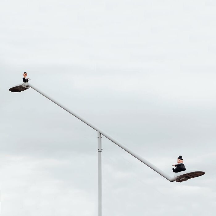 Street art featuring a character playing a flute atop a modern street lamp, showcasing public space creativity by Frankey.