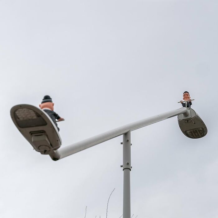 Street art featuring a character playing a flute atop a modern street lamp, showcasing public space creativity by Frankey.