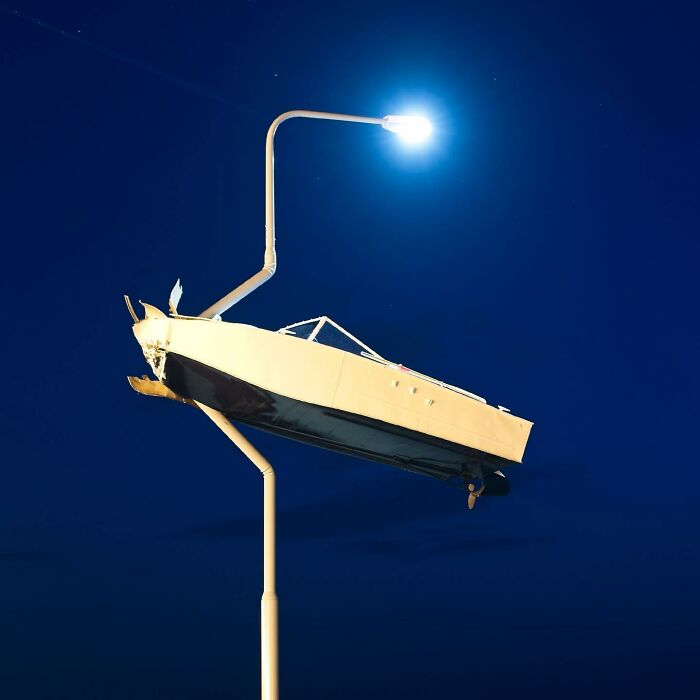 Street art showing a boat mounted on a lamp post on the beach with a dog standing nearby at sunset.