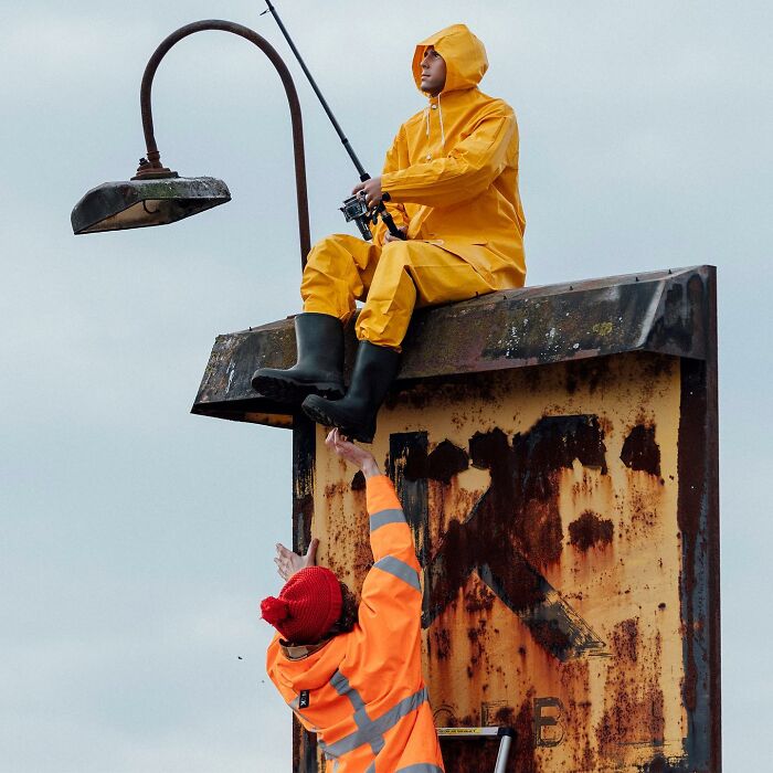 Street art installation by Frankey showing a person in yellow rain gear fishing from a rusty urban structure.