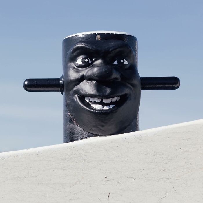 Black street art bollard with a smiling face creatively transforming public spaces through clever street art by Frankey.