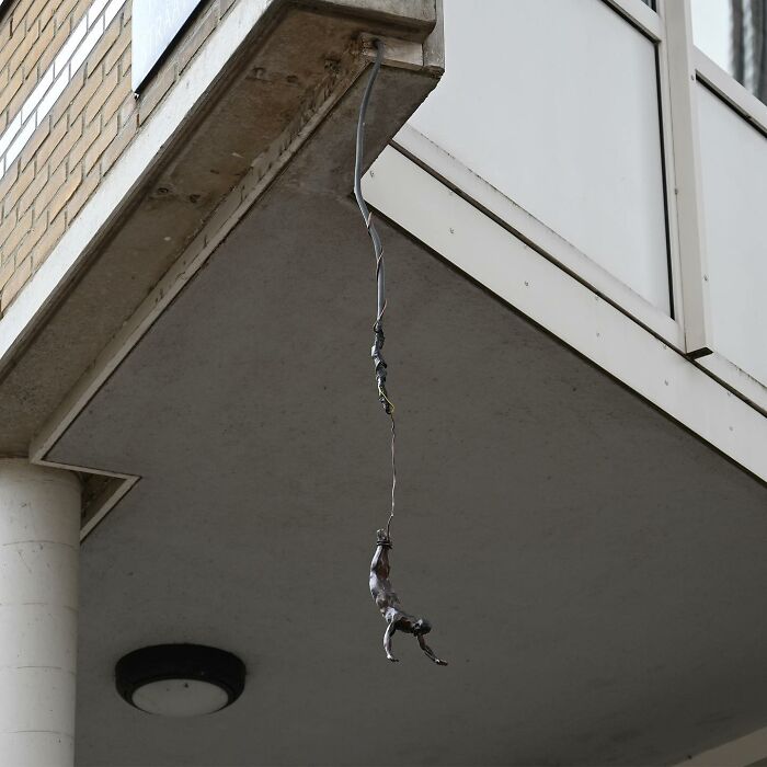 Small street art sculpture of a climber hanging from a wire, showcasing clever interpretations of public spaces by Frankey.