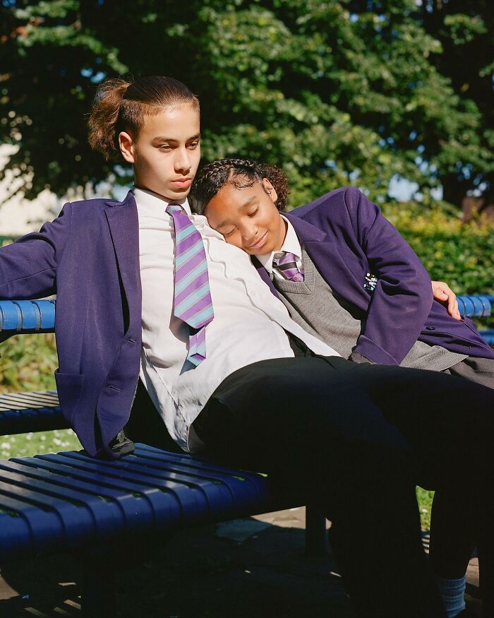 Two schoolchildren in uniform resting on a bench, captured in honest photos of London by Nico Froehlich.