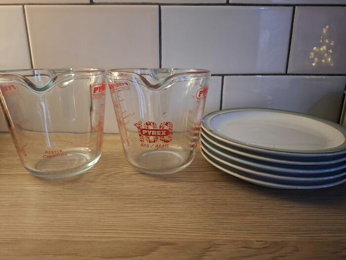 Two glass Pyrex measuring cups and a stack of white plates on a wooden countertop showing real-life glitches in the matrix.
