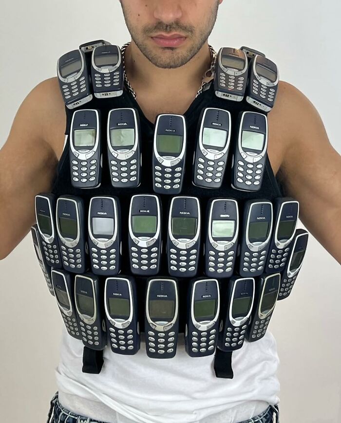 Man wearing a vest covered in vintage Nokia phones, combining trash and culture in a chaotic and humorous display.