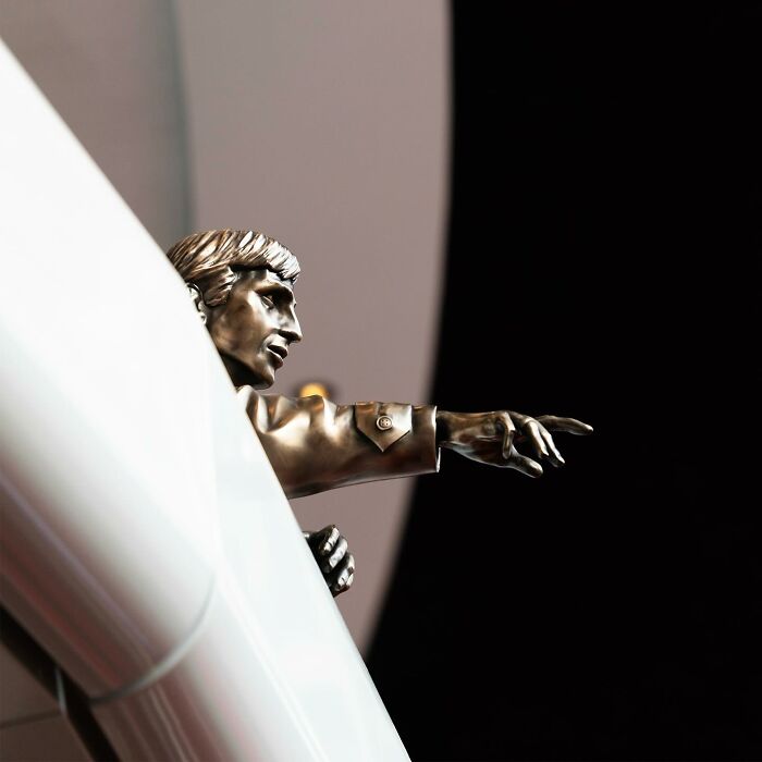 Bronze street art sculpture by Frankey creatively interacting with public space in a stadium setting.