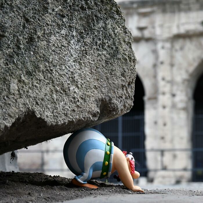 Street art interpretation of public spaces showing a cartoon figure pushing a giant stone near the Colosseum.