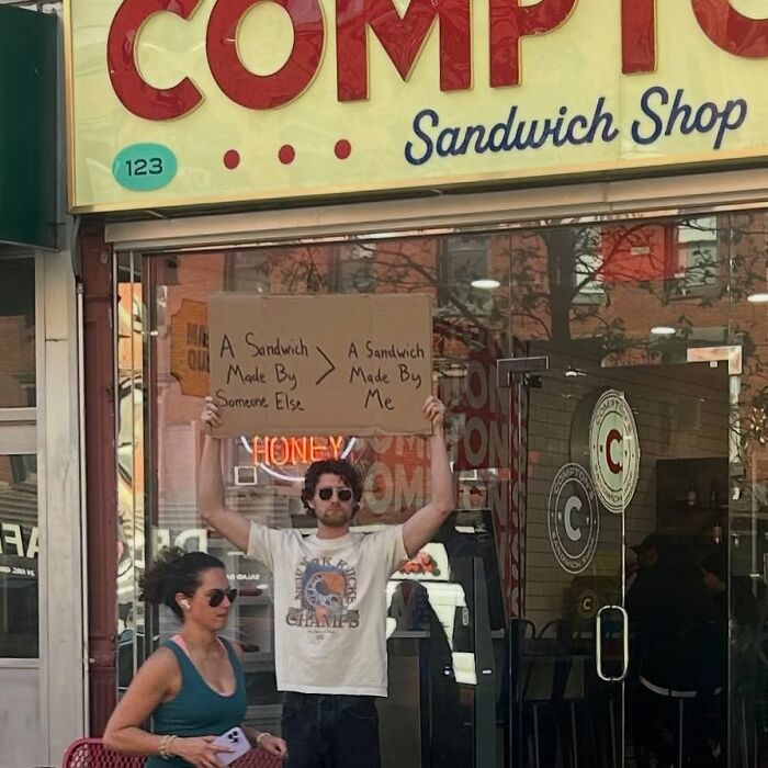 Man holding a sign outside a sandwich shop, a dude with the sign showing relatable funny messages.