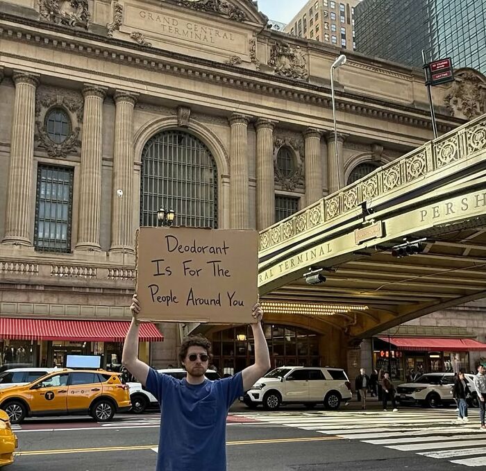 Man holding sign about deodorant in front of Grand Central Terminal, reflecting dude with the sign’s witty public messages.