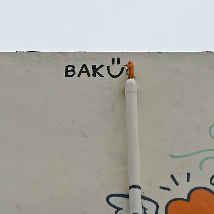 Street art interpretation of public spaces showing a small orange figure painting a smiley on an urban wall.