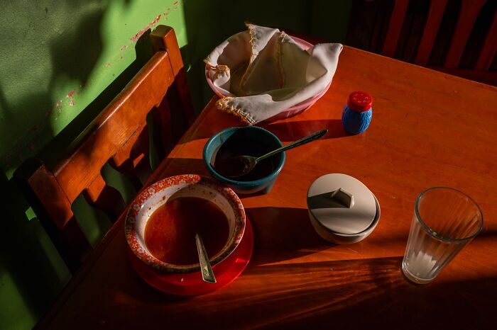 Empty wooden chair and table with soup bowl, bread basket, condiments, and glass, capturing honest street moments.