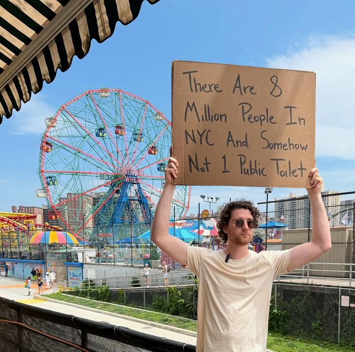Man holding a cardboard sign at amusement park, example of Dude With The Sign sharing witty public thoughts in NYC.