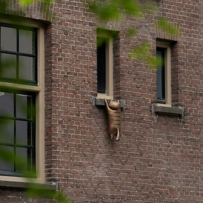 Bronze cat sculpture cleverly integrated into public space on a brick building as street art by Frankey.