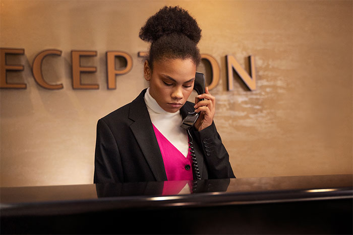 Hotel receptionist on phone handling a complaint about an obnoxious Karen using the hotel pool after closure. - 7