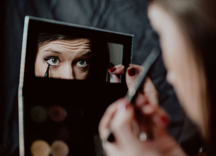 Woman applying makeup using a compact mirror, focusing on eyeliner, with niece’s makeup treated like Sephora products. - 10