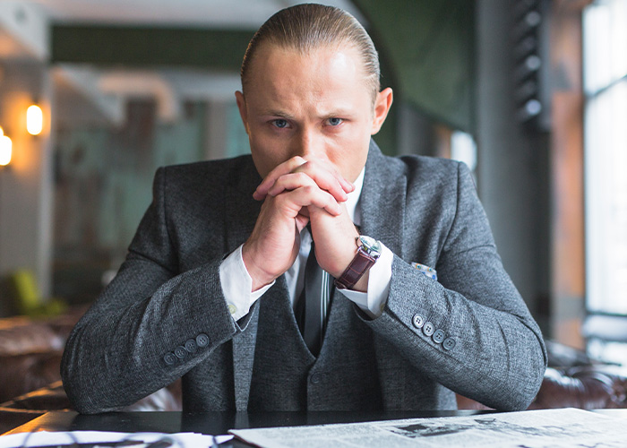 Serious man in a gray suit sitting at desk, reflecting on ridiculous complaints managers and HR received from employees.