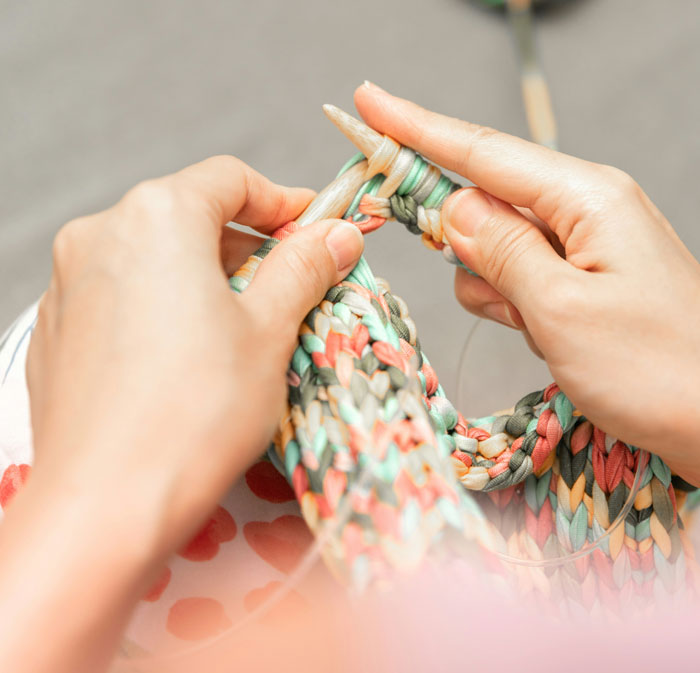 Hands knitting a colorful fabric, illustrating unexpected things people learned about the rich through interaction.