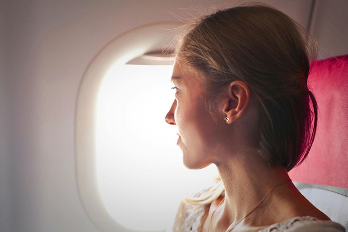 Woman looking out airplane window, reflecting on feminist perspectives about holding doors open for big burly men.